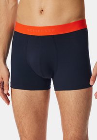 Tengeréskék boxer alsónadrág narancssárga gumírozott derékkal, sima textúrával és szoros illeszkedéssel, kiemelve a formázott kialakítást.