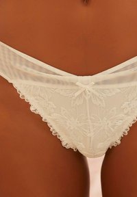 Elfenbeinfarbene Spitzen-Slips mit floralem besticktem Muster, gewellten Kanten und einer Satinschleife am Bund, ergänzt durch transparente Mesh-Details.