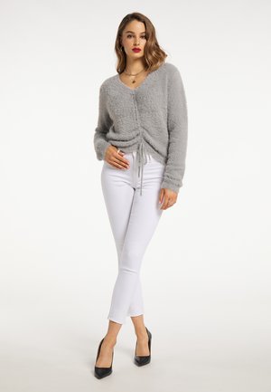 Grå, fluffy v-hals sweater med snøresnordetalje, båret med hvide skinny jeans og sorte spidse hæle. Glat tekstur, afslappet pasform.