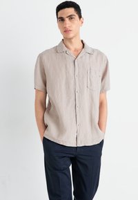 Krátkožírková, button-up košela z svetlo béžového ľanu s nápršnou kapsou. Skombinovaná s tmavými nohavicami pre voľný strih.