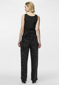 Haut noir sans manches avec un col rond associé à un pantalon noir pailleté et des chaussures à plateforme noires. Matières lisses et texturées.