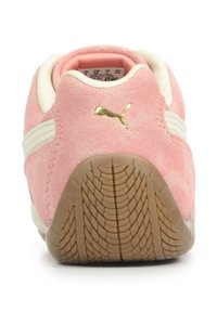 Sneakers Puma in morbido suede rosa chiaro con strisce bianche, logo dorato e suola in gomma testurizzata. Forma arrotondata e colletto imbottito per il comfort.