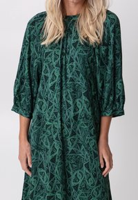 Vestido verde con estampado que presenta un corte holgado, mangas de 3/4 y un escote redondo, con intrincados remolinos y texturas en toda su superficie.
