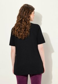 Camiseta negra de manga corta con un ajuste holgado, fabricada en tejido suave, mostrada desde la parte de atrás. Combinada con pantalones morados.