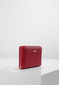 Rood leren portemonnee met een textuurfinish, gouden rits en merklgo. Vierkante vorm, compact ontwerp, voorzien van een ritssluiting voor extra beveiliging.
