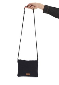 Sac en bandoulière rectangulaire bleu marine en tissu doux, avec une étiquette en cuir et des sangles noires ajustables.