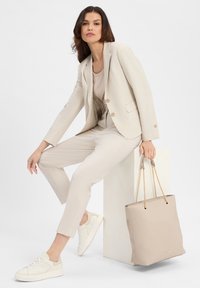 Blazer e pantaloni beige in tessuto texturizzato, abbinati a un top beige e sneaker bianche. Una borsa a tracolla beige chiaro con dettagli in catena.