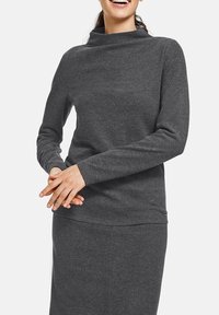 Dunkelgraues Longsleeve-Oberteil mit Trichterkragen, aus glattem, weichem Stoff gefertigt. Figurumspielendes Design mit subtiler Naht und minimalistischem Akzent.