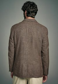 Braun strukturierter Blazer mit klassischem Schnitt, der ein dezentes Hahnentritt-Muster und Ein-Knopf-Manchetten aufweist, von hinten gezeigt.
