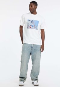 Witte T-shirt met een kleurrijke basketbalk graphic, gecombineerd met lichtblauwe, losse jeans en witte sneakers met grijze details.