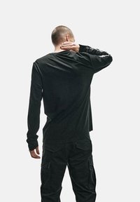 Czarna koszulka z długim rękawem wykonana z miękkiego materiału, z okrągłym dekoltem, luźnym krojem i białym napisem na prawym rękawie.