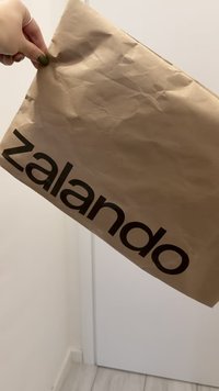 Barna papír bevásárlótáska, amelyen a "zalando" logó nagy, vastag, fekete betűkkel látható. A táska gyűrődéseket és az újrahasznosított papírra jellemző textúrát mutat.