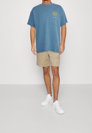 T-shirt en coton bleu avec un col rond et des manches courtes, assorti à un short beige. Complété par des baskets blanches pour un look décontracté.