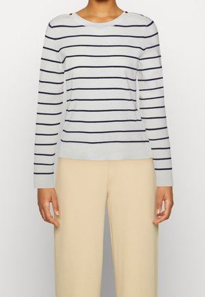 Pull rayé gris clair avec des lignes marine, encolure ronde, manches longues et boutons sur les épaules. Associé à un pantalon à jambes larges beige.