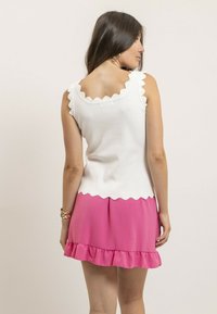 Top blanc sans manches avec des bords festonnés au niveau du col et de l'ourlet, associé à une jupe rose avec des volants. Textures lisses, design décontracté.