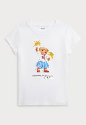 Biała koszulka z misiem w niebieskiej spódnicy, białym swetrze z amerykańską flagą, trzymającym żółte kwiaty, oraz napisem Polo Bear by Ralph Lauren poniżej.