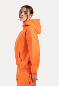 Sudadera con capucha de mezcla de algodón en un vibrante color naranja, con un bolsillo frontal, puños acanalados y un parche con el logo en el pecho.