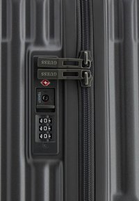 Zwarte koffer met ribbelige harde schaal, dubbele ritssluitingen, TSA-goedgekeurd slot en combinatie-draaiknop aan de voorkant, textuur voor grip.