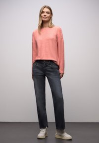 Jasnoróżowy sweter z długimi rękawami i guzikami na ramionach, połączony z ciemnoniebieskimi prostymi dżinsami i białymi trampkami.