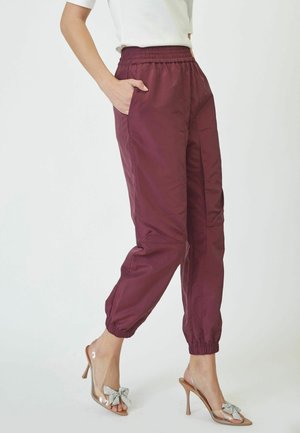 Burgundy jogger pants with an elastic waistband, side pockets, and cuffed ankles, made from a smooth, lightweight material.