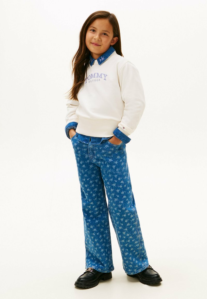 Felpa bianca con logo "TOMMY HILFIGER", colletto di camicia in denim blu, jeans con fantasia floreale blu e scarpe nere. Fit rilassato.