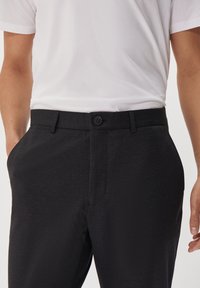 Svarta byxor av texturerat tyg med knappstängning, sidofickor och skräddarsydd passform, kombinerade med en enkel vit t-shirt.