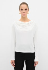 Witte lange mouwtop met een gedrapeerde halslijn, gemaakt van een gladde, lichte stof. Gepromoot met zwarte aangesloten broeken, minimalistisch ontwerp.