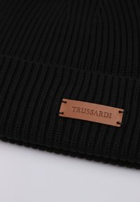 Czarna prążkowana czapka typu beanie wykonana z dzianiny, z brązową skórzaną metką z wytłoczonym napisem "TRUSSARDI." Czyste krawędzie o miękkiej fakturze.