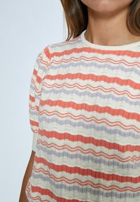 Top a righe in maglia con onde corallo, lavanda e bianche, caratterizzato da un motivo testurizzato. Maniche corte e scollatura rotonda.