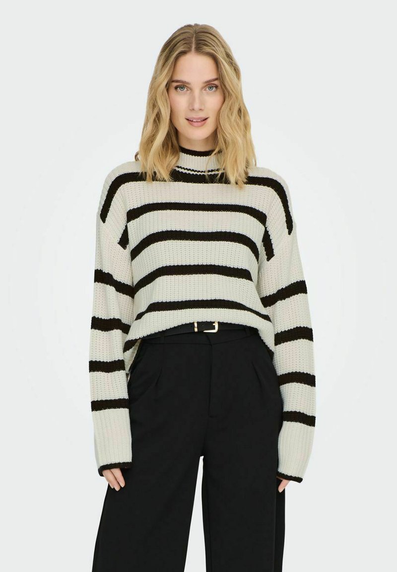 Gestreifter Strickpullover in Creme und Schwarz, mit hohem Kragen und langen Ärmeln. Über einer schwarzen, hoch taillierten Hose getragen.