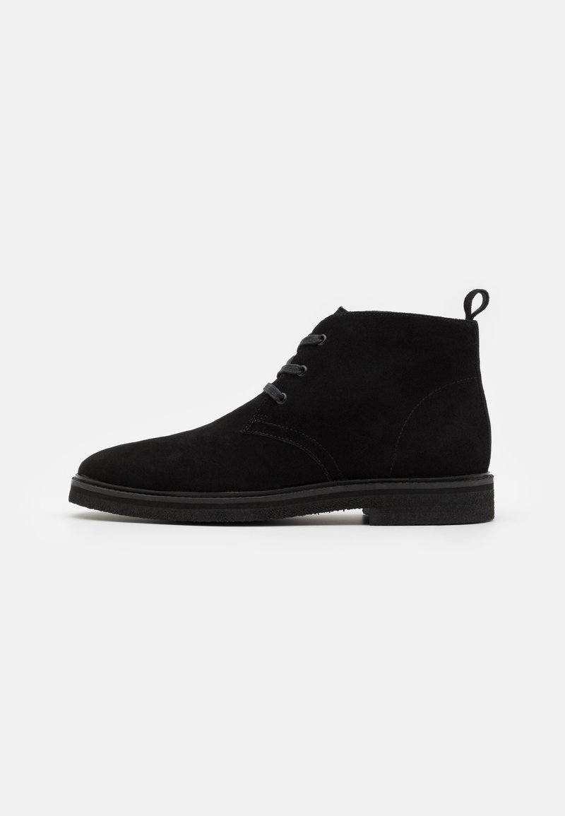 Botines de ante negro con puntera redondeada, dos ojales para los cordones y una pequeña lengüeta en la parte posterior. Suela de goma plana.