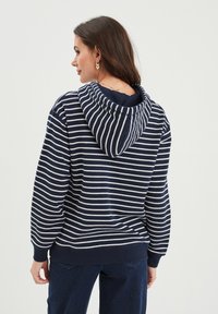 Felpa a righe blu navy e bianche con un grande cappuccio, polsini e orlo a costine. Tessuto morbido con una vestibilità rilassata, progettata per il comfort e l'abbigliamento casual.