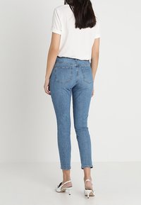 Blå denim jeans med slim fit, medelhög midja, bakfickor och en vit t-shirt med uppvikta ärmar, i kombination med vita klacksandaler.