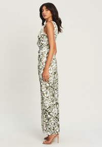 Floral jumpsuit in olive green and white, featuring a fitted bodice, side tie detail, and wide pant legs; smooth fabric texture.