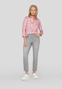Farbenfrohe gemusterte Bluse in Pink, Orange und Weiß; graue Slim-Fit-Jeans; weiße Sneaker; Oberteil mit dreiviertel Ärmeln.