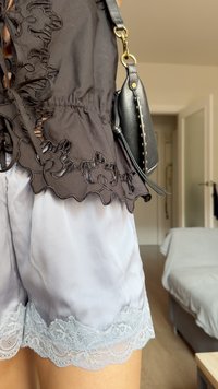 Top in tessuto nero con ritagli floreali e orlo arricciato abbinato a pantaloni corti di satin grigio chiaro con merletto in fondo. Borsa nera con borchie.