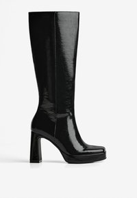 Botte haute noire en cuir verni avec talon bloc et bout légèrement carré, vue de profil sur fond blanc.