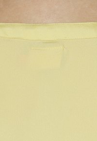 Un tissu jaune avec une texture lisse et brillante présente une petite poche cousue à l'arrière, mettant en avant un design simple et un matériau léger.