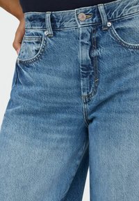 Jeans in denim blu a vita alta con una finitura sbiadita, dotati di tasche frontali, chiusura con bottone di metallo e dettagli di cucitura a contrasto.