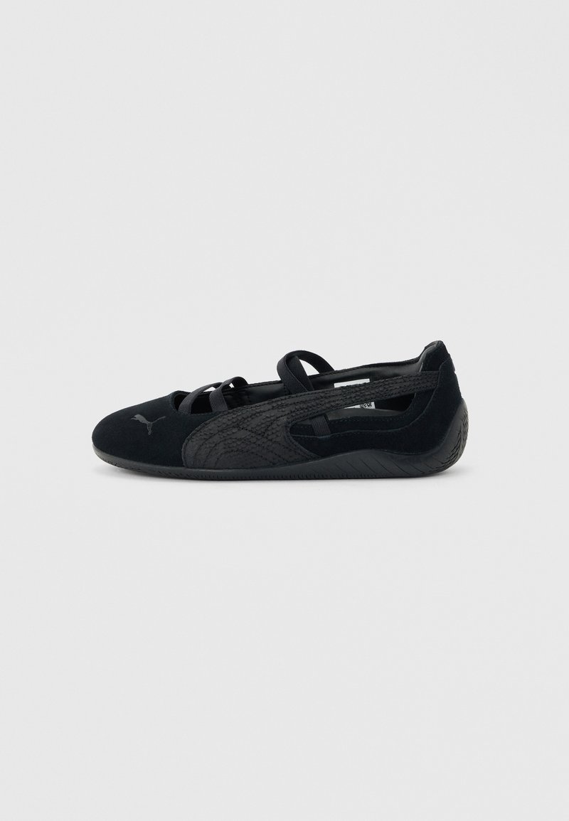 Chaussure plate style ballet noire avec des brides croisées, logo Puma texturé sur le côté et semelle en caoutchouc flexible sur fond neutre.