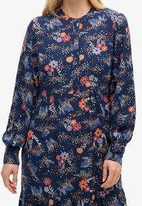 Abito floreale navy con maniche lunghe, colletto con bottoni e design a strati con motivi di fiori rossi, blu e bianchi.