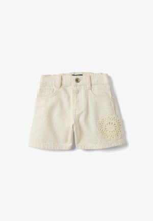 Pantalones cortos para niños pequeños color crema con bolsillos delanteros, cierre de botón, trabillas para cinturón y un parche decorativo de crochet en la pierna derecha.