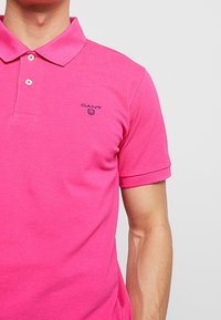 Polo rosa realizzato in cotone, con colletto, maniche corte e un piccolo logo ricamato sull'area sinistra del petto.
