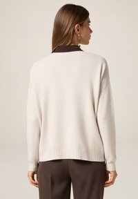 Cremefarbener Pullover aus weichem Strickmaterial mit lockerer Passform, Rippenmuster am Saum und an den Bündchen, mit einem kontrastierenden braunen Kragen.