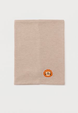 Carré de tissu beige en maille gaufrée avec un petit visage de lion orange brodé près du coin inférieur droit.