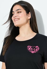 Zwart t-shirt met korte mouwen en een roze beerafbeelding op de linkerborst. Gladde, lichte stof met een ronde halslijn.