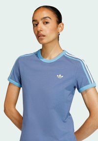 Jasnoniebieska bawełniana koszulka z okrągłym dekoltem, krótkimi rękawami i białymi paskami na ramionach. Zawiera małe logo na piersi.