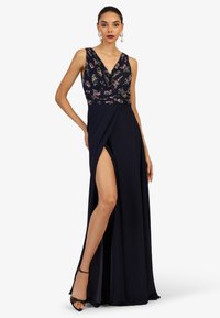 Marineblaues Kleid mit floraler Musterung am Oberteil, tiefem V-Ausschnitt und einem hohen Schlitz am Bein. Hergestellt aus glattem Stoff, mit tailliertem Bund und drapiertem Rock.