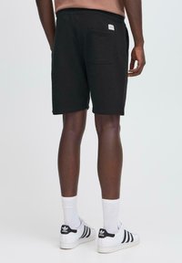 Zwarte katoenen shorts van een katoenmix met een tailleband en een achterzak. Het model draagt witte en zwarte sneakers en crewlength witte sokken.