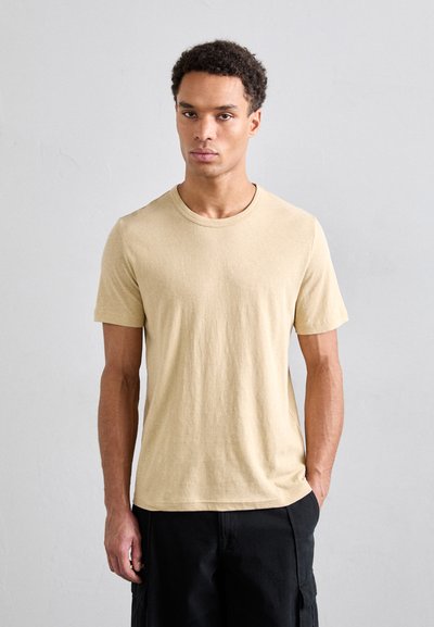 T-shirt en coton beige à manches courtes et encolure ras du cou. Texture douce, coupe régulière, associé à un short cargo noir.